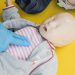 A person demonstrates infant CPR on a manikin, highlighting first aid techniques.